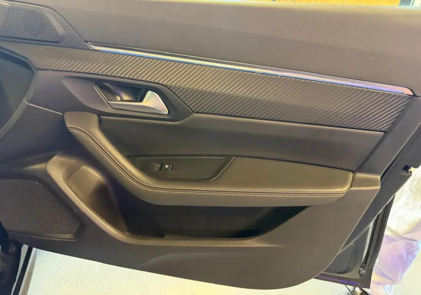 Intérieur côté gauche de porte avant noir avec insert carbone et surpiqûres blanches sur Peugeot 508 SW 2024.
