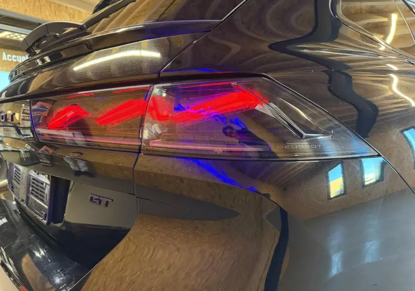 Gros plan sur le feu arrière droit rouge d’une Peugeot 508 SW GT noire brillante, avec badge GT visible.