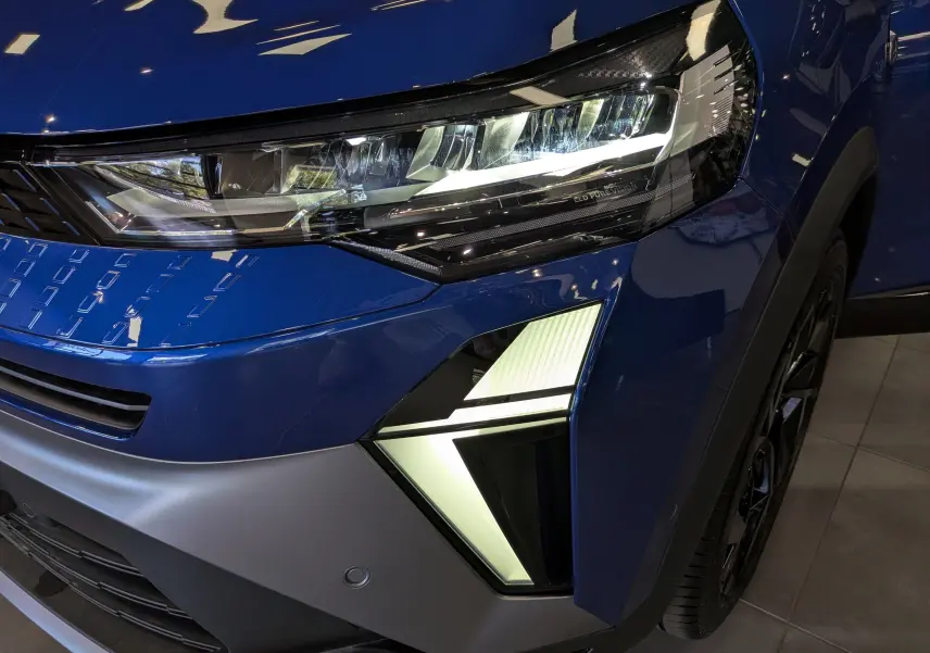 Gros plan sur le phare avant droit allumé du Renault Captur E-Tech bleu Iron avec détails lumineux distinctifs.