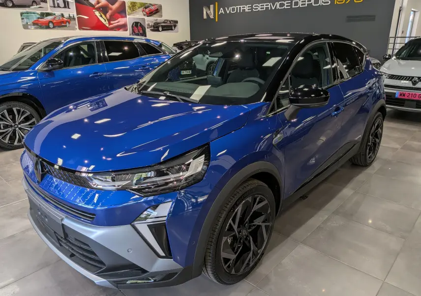 Renault Captur E-Tech hybride 2026 bleu Iron avec toit noir, vue 3/4 avant droit en showroom intérieur.