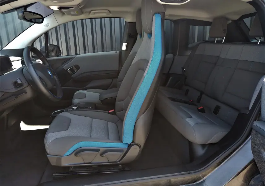 Intérieur de la BMW i3 bleu, vue côté gauche montrant les sièges avant et arrière en tissu gris avec surpiqûres bleues.