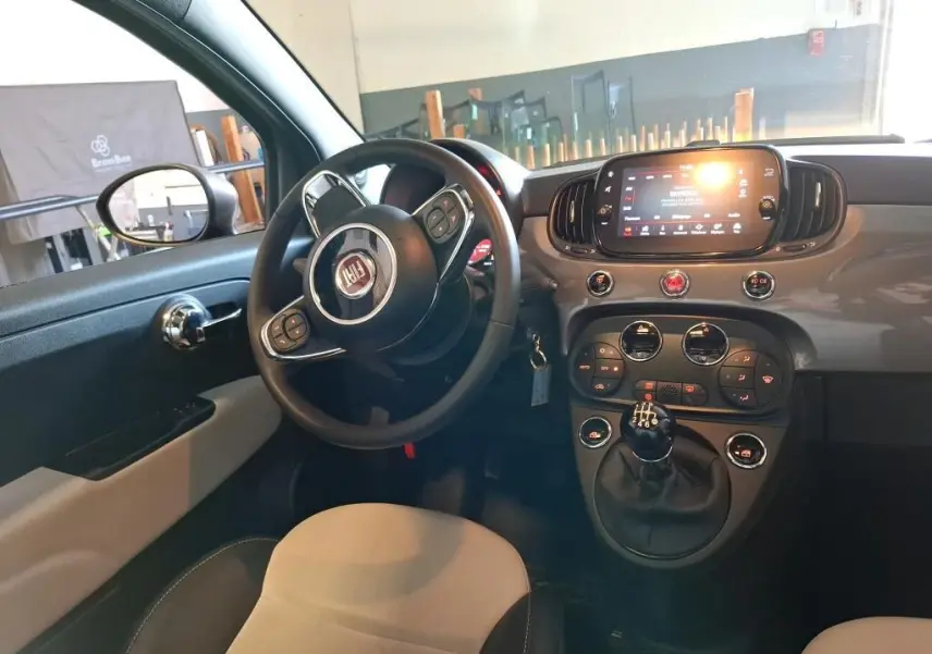 Intérieur du Fiat 500 2022 vu côté conducteur, tableau de bord gris Electroclash avec écran tactile et levier de vitesse manuel.