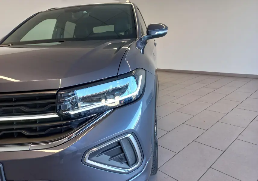 Vue rapprochée 3/4 avant droit du Volkswagen T-Cross gris cendré, mettant en valeur le phare LED et la calandre chromée.