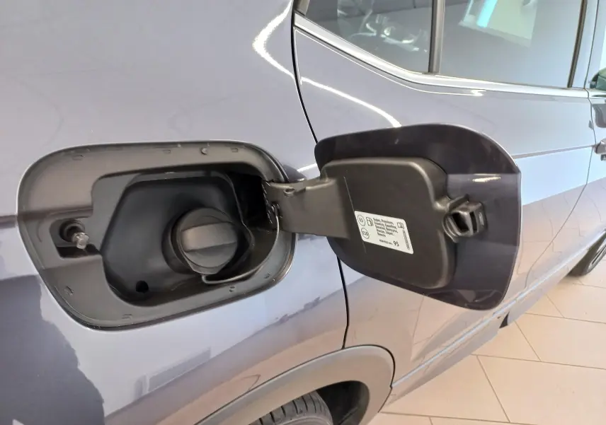 Gros plan sur la trappe à carburant ouverte côté gauche d'un Volkswagen T-Cross 2025 gris cendré avec jantes alliage visibles.