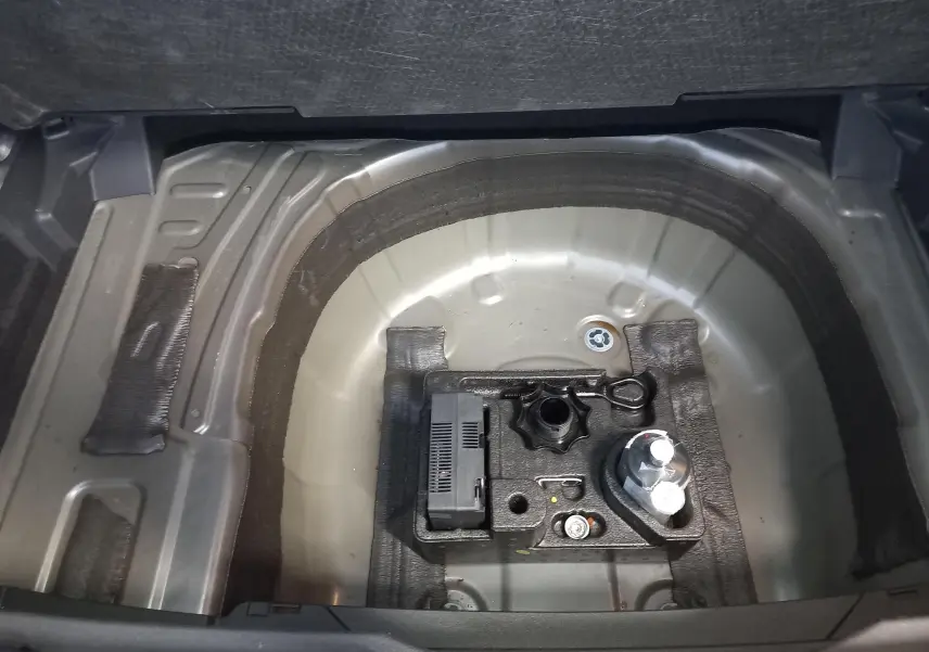 Vue intérieure du coffre du Volkswagen T-Cross gris cendré, montrant le rangement sous plancher sans roue de secours.