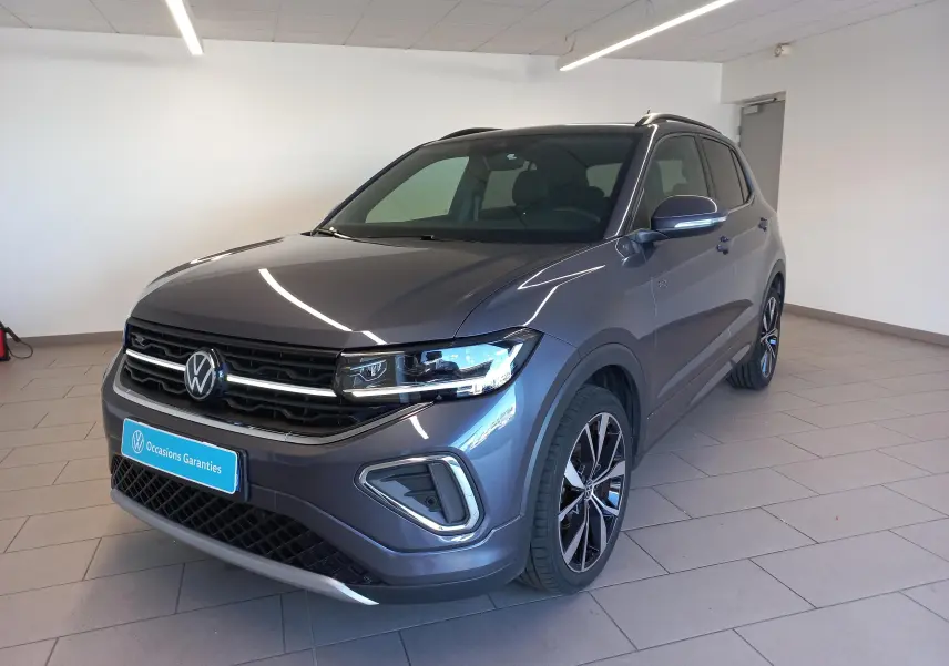 Volkswagen T-Cross gris cendré en 3/4 avant droit, avec jantes alliage 18 pouces et finition R-Line visible.