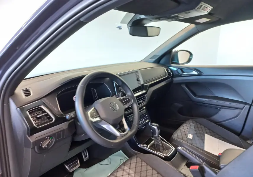 Vue intérieure côté conducteur du Volkswagen T-Cross 2025, tableau de bord noir avec volant multifonction et sellerie tissu à motifs.