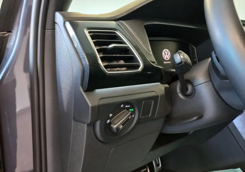 Détail intérieur côté gauche du tableau de bord du Volkswagen T-Cross gris cendré, avec commande des phares et aérateur.