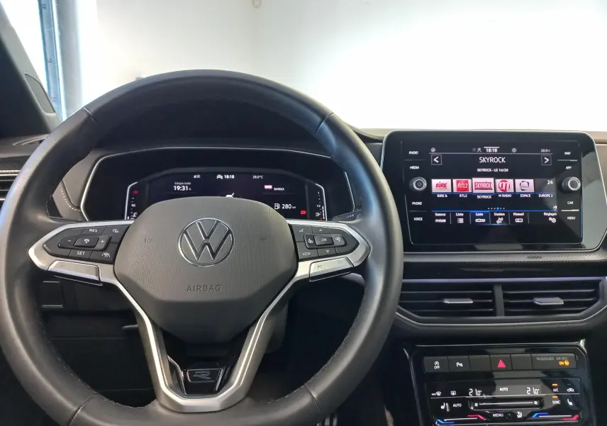 Vue intérieure centrée sur le volant noir du Volkswagen T-Cross 2025 avec tableau de bord digital et écran tactile multimédia.