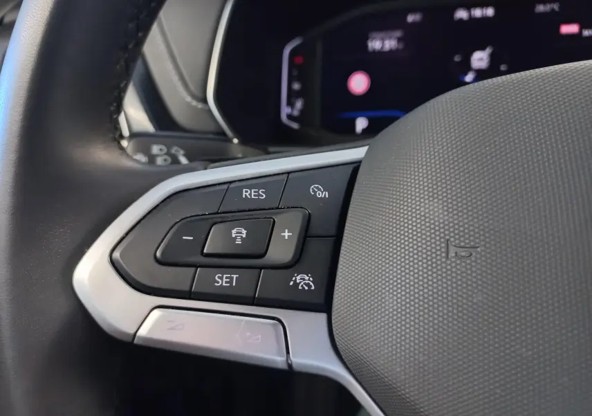 Gros plan sur les commandes au volant côté gauche du Volkswagen T-Cross 2025, finition R-Line, avec boutons de régulateur de vitesse.
