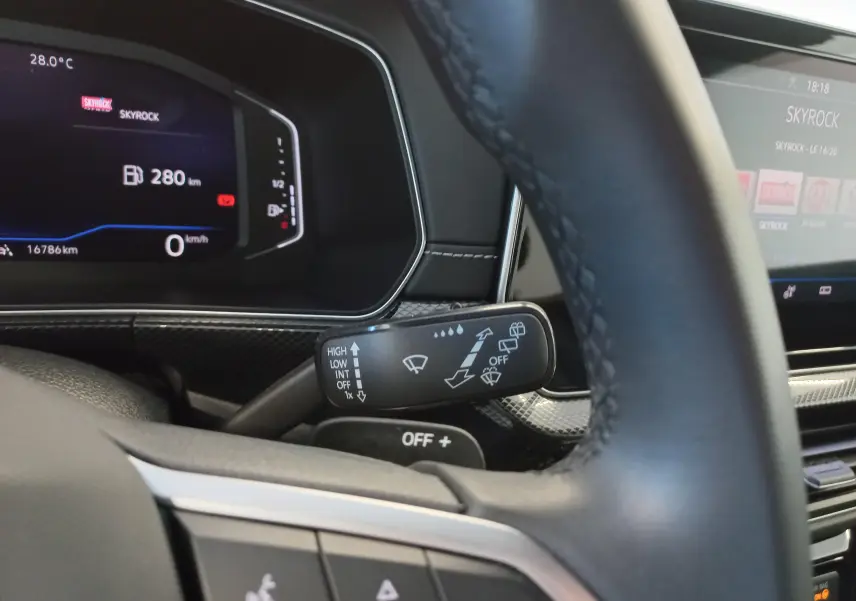 Vue rapprochée du commodo d’essuie-glace derrière le volant d’un Volkswagen T-Cross gris cendré, tableau de bord numérique en arrière-plan.