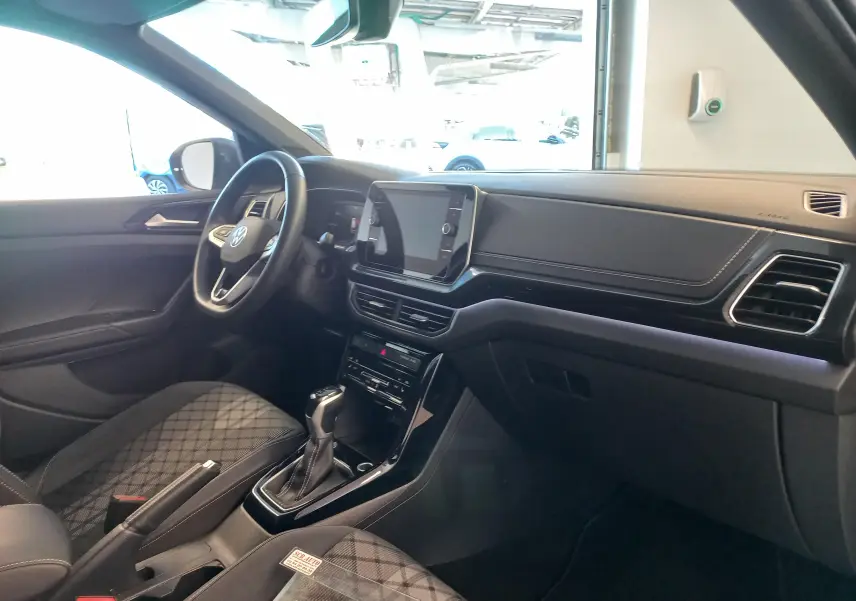Vue intérieure côté conducteur du Volkswagen T-Cross 2025, avec tableau de bord moderne et sellerie tissu à motif.
