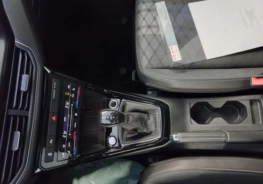Vue intérieure centrée sur la console centrale du Volkswagen T-Cross 2025, avec levier de vitesse DSG et sièges tissu gris.