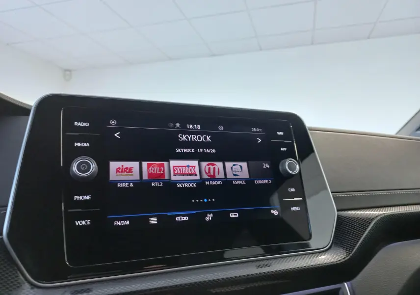 Vue intérieure du tableau de bord du Volkswagen T-Cross 2025 avec écran tactile affichant les stations radio, finition R-Line en gris cendré.