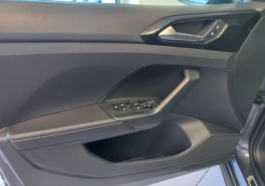 Vue intérieure côté gauche de la porte avant d'un Volkswagen T-Cross gris cendré avec commandes électriques des vitres.
