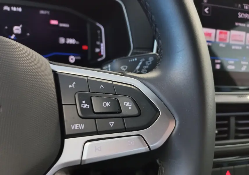 Gros plan sur les commandes au volant côté gauche du Volkswagen T-Cross 2025 gris cendré, version R-Line Edition.