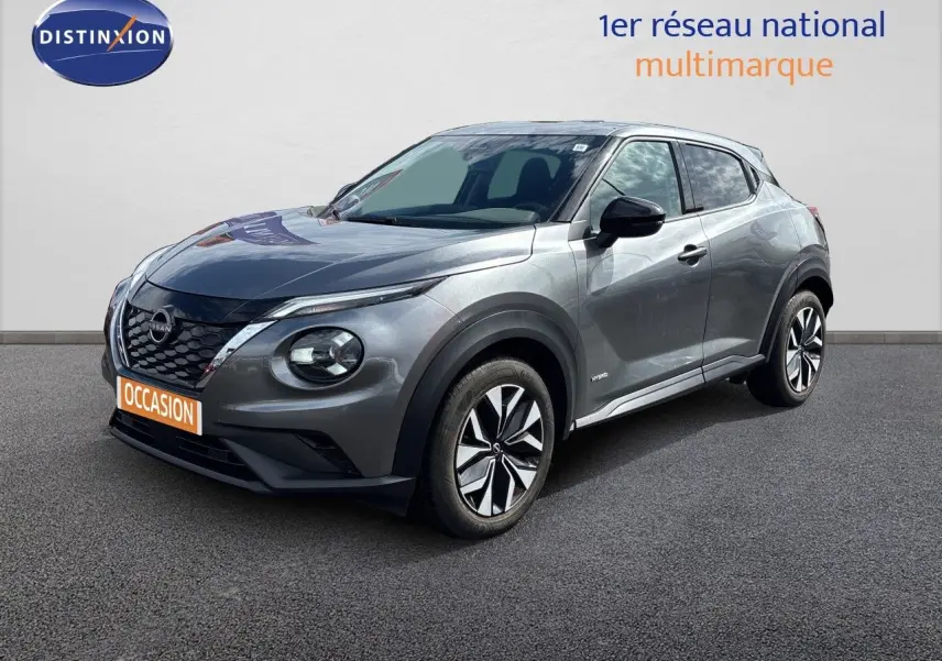 Nissan Juke Hybrid gris squale métal en 3/4 avant droit, avec jantes modernes et calandre noire distinctive.