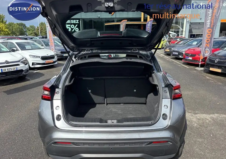 Vue arrière du Nissan Juke Hybrid 143ch Business Edition gris squale métal avec coffre ouvert sur parking extérieur.