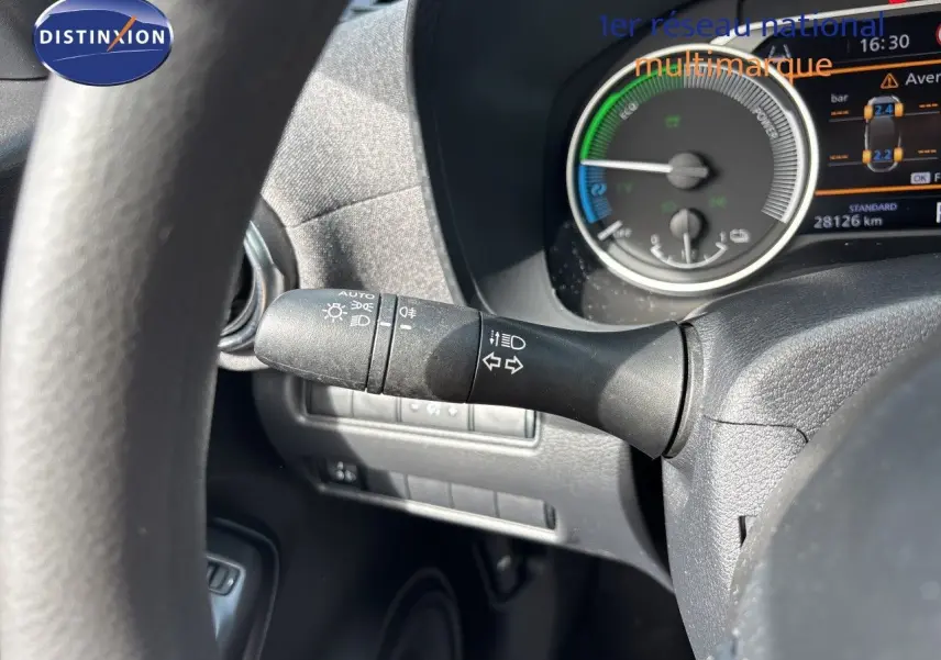 Gros plan sur les commandes au volant noir du Nissan Juke Hybrid 2024, avec tableau de bord et aérateur circulaire en arrière-plan.