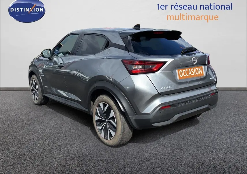 Nissan Juke Hybrid gris squale métal vu de profil côté gauche, avec jantes alliage et lignes dynamiques marquées.