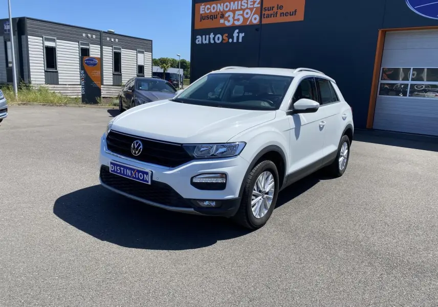 Volkswagen T-Roc blanc pur en 3/4 avant droit, avec calandre noire et jantes alliage visibles sur parking extérieur.