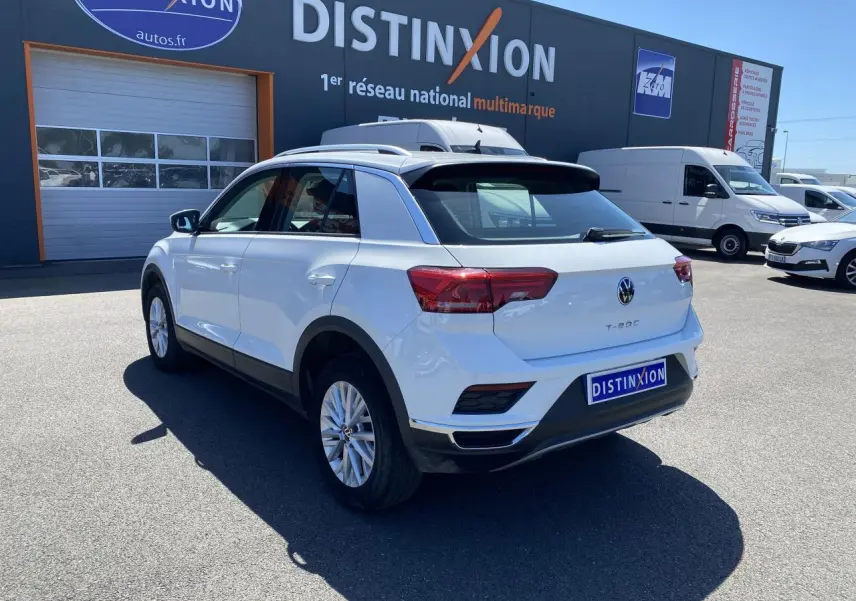 Volkswagen T-Roc blanc pur vu en 3/4 arrière droit, stationné devant un bâtiment avec logo Distinxion.
