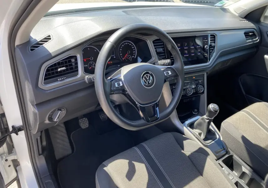 Vue intérieure côté conducteur du Volkswagen T-Roc blanc pur 2021, volant cuir et levier de vitesse manuel visibles.