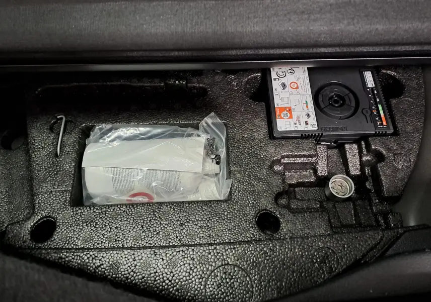 Rangement sous plancher de coffre du Volkswagen Touran 2025, avec kit de réparation pneu et mousse noire texturée.