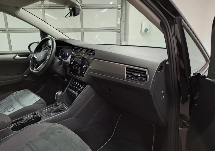 Vue intérieure côté conducteur du Volkswagen Touran 2025 noir grenadille, avec sellerie Alcantara et tableau de bord moderne.