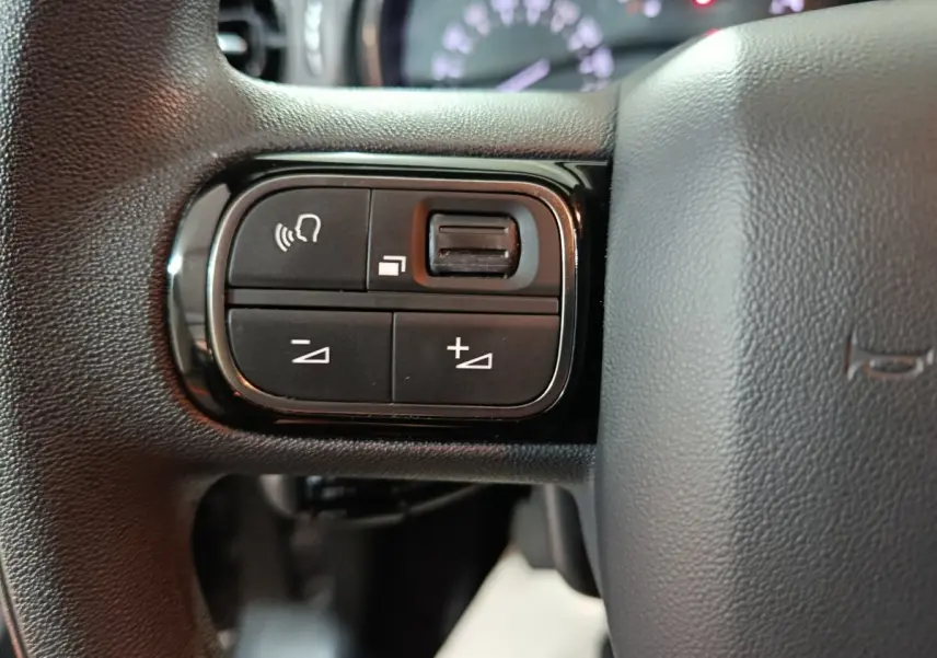 Gros plan sur les commandes multifonctions noires à gauche du volant gris foncé du Citroën C3 2024.