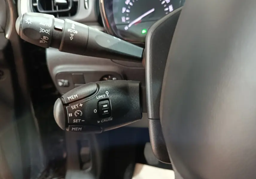 Gros plan sur les commandes de régulateur et limiteur de vitesse à gauche du volant dans une Citroën C3 gris foncé 2024.