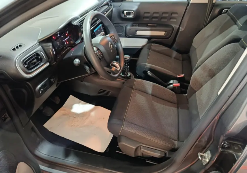 Intérieur avant droit de la Citroën C3 gris foncé 2024, avec tableau de bord et sièges tissu noirs.