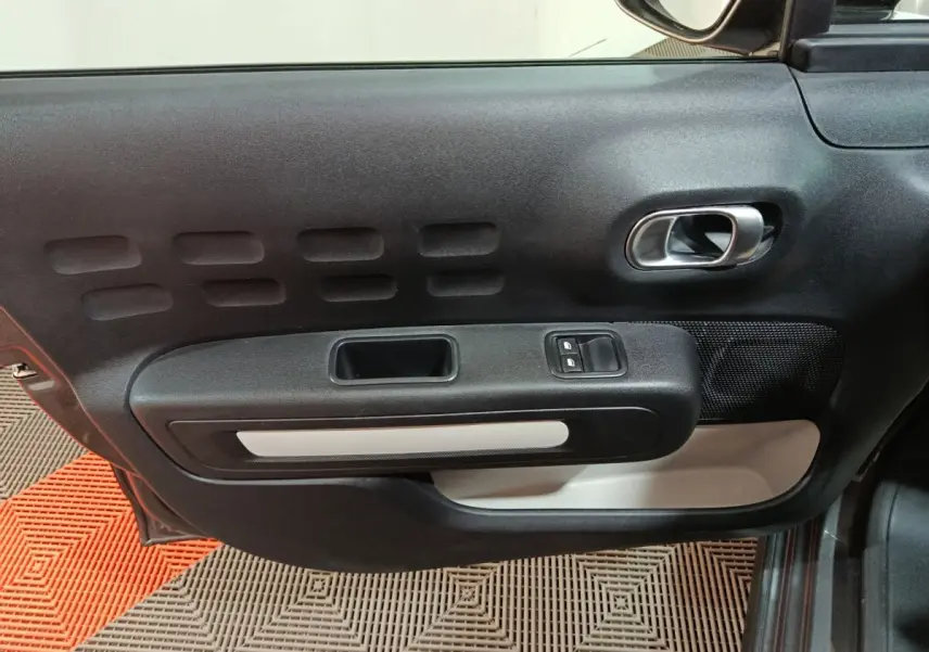 Vue intérieure côté gauche de la porte avant d'une Citroën C3 2024 gris foncé avec commandes de vitres et poignée argentée.