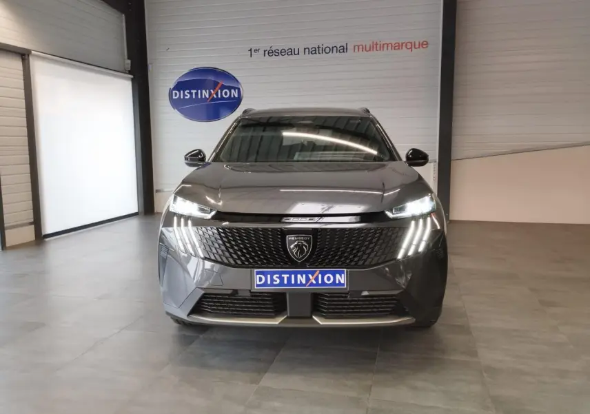 Vue de face du Peugeot 5008 gris titanium 2025 avec calandre noire et feux LED distinctifs allumés.