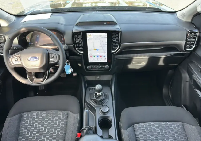 Vue intérieure avant du Ford Ranger 2025, tableau de bord noir avec écran tactile vertical et boîte manuelle.