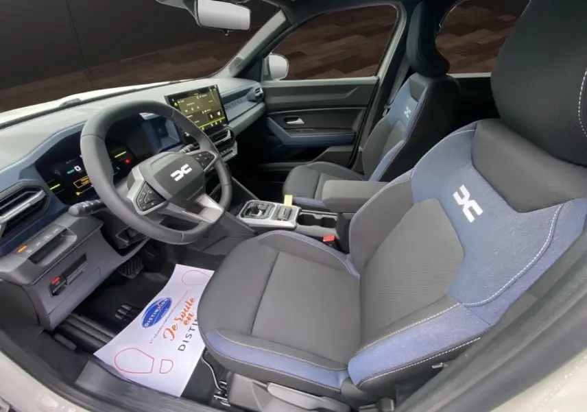 Intérieur du Dacia Duster Journey Hybrid 140 vu côté conducteur, sièges tissu noir et bleu avec logo blanc.