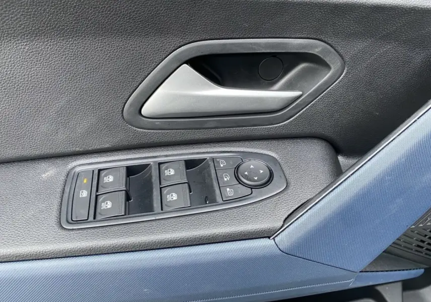 Détail des commandes de lève-vitres et rétroviseurs sur la portière côté conducteur d'un Dacia Duster beige.