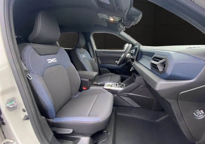 Vue intérieure côté conducteur du Dacia Duster beige 2025, sièges tissu noir et bleu avec logo DC brodé.