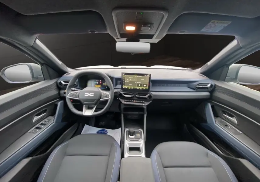 Vue intérieure avant du Dacia Duster Journey Hybrid 140, tableau de bord moderne avec écran tactile central et volant multifonctions.