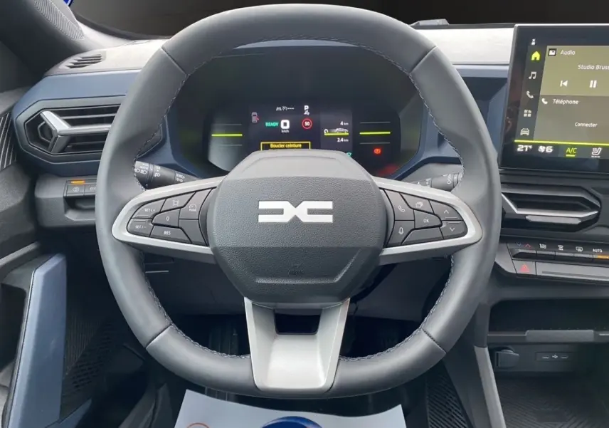 Vue intérieure centrée sur le volant cuir noir du Dacia Duster Journey Hybrid 140 avec tableau de bord digital et écran tactile.
