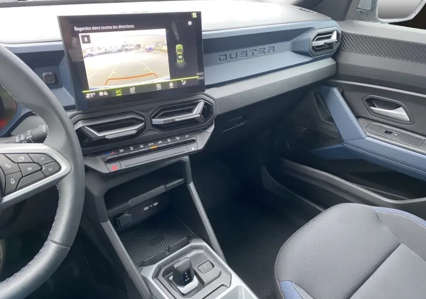 Vue intérieure côté passager du tableau de bord et console centrale du Dacia Duster beige avec écran tactile et volant multifonctions.