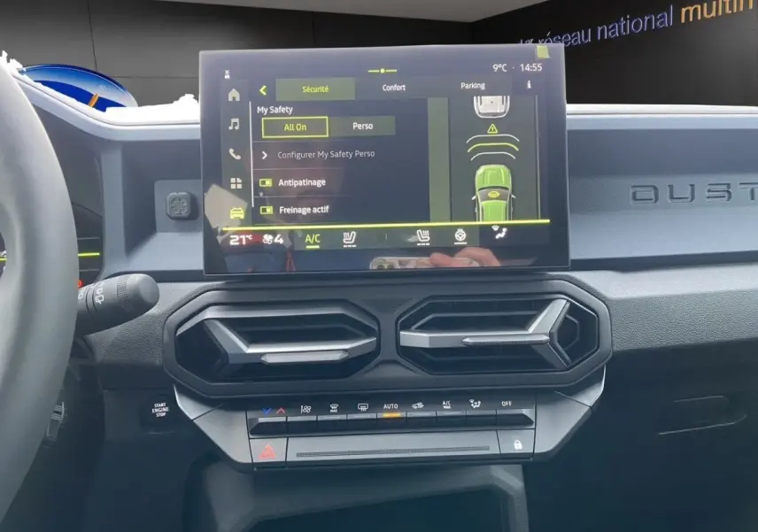 Vue intérieure du tableau de bord du Dacia Duster beige 2025, avec écran tactile central et commandes climatisation.