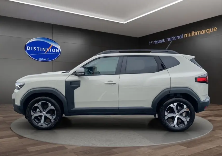 Vue de profil côté gauche du Dacia Duster beige 2025 avec jantes alliage et protections noires sur les passages de roue.