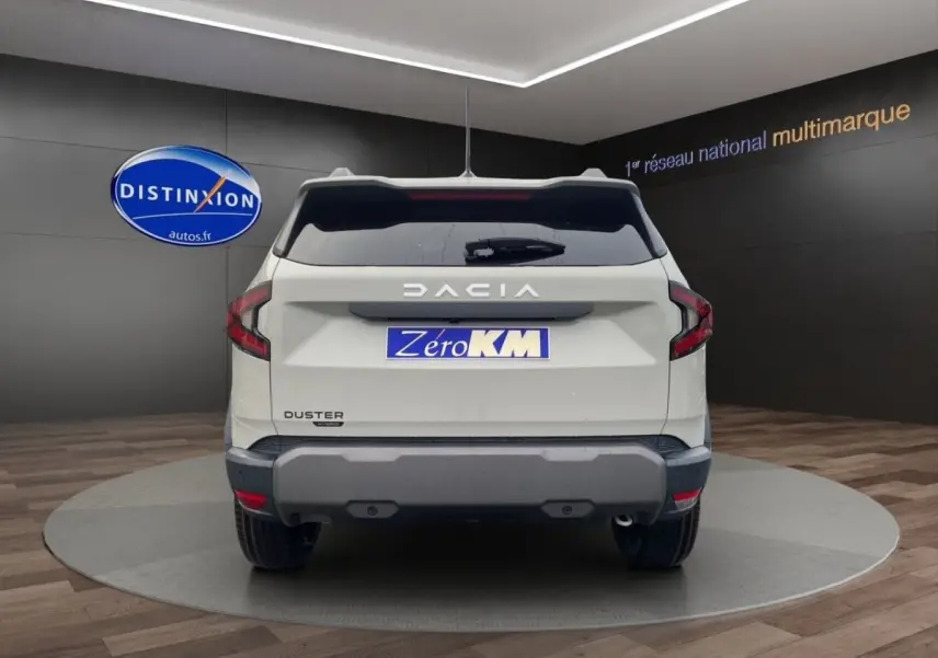 Vue arrière d'un Dacia Duster beige 2025 avec logo DACIA lumineux et plaque Zero KM dans un showroom.