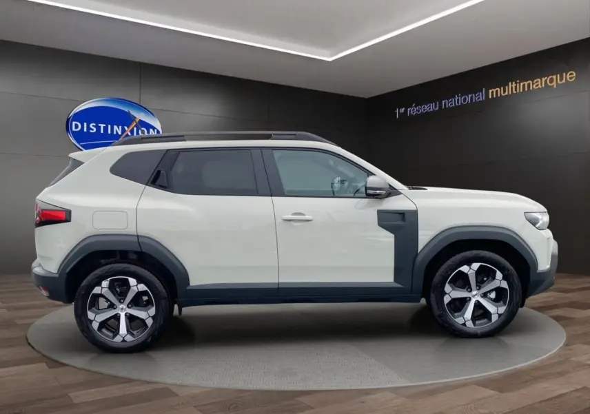 Vue latérale droite du Dacia Duster beige 2025 avec jantes alliage et protections noires contrastantes.