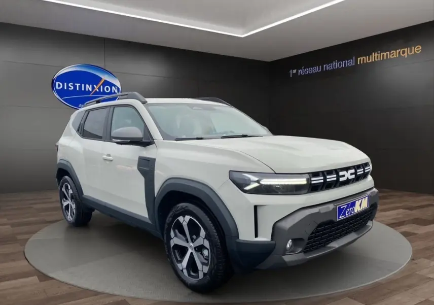 Vue 3/4 avant d'un Dacia Duster beige 2025 avec phares LED et jantes alliage distinctives.