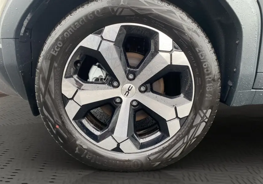 Gros plan sur la jante noire et argentée d’un Dacia Duster beige, avec pneu Continental sous la pluie.