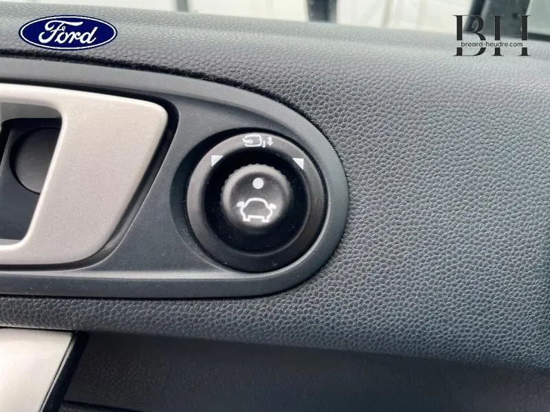Gros plan sur la commande de réglage des rétroviseurs côté conducteur dans l’habitacle gris foncé d’une Ford Fiesta 2012 Titanium.