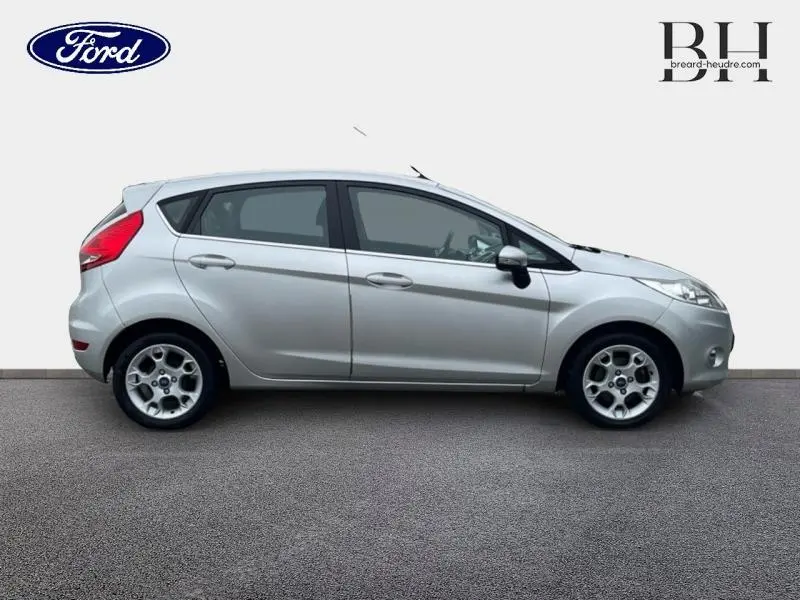 Vue de profil droit d'une Ford Fiesta gris lunaire 2012 avec jantes alu 15 pouces et vitres teintées.