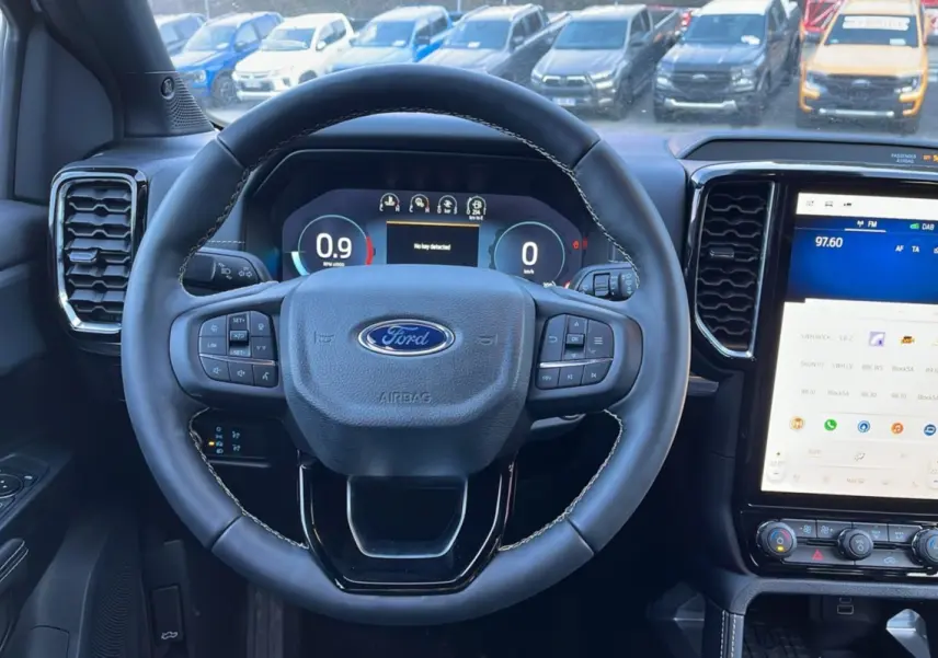 Vue intérieure centrée sur le volant cuir multifonctions du Ford Ranger 2025, avec écran tactile vertical et tableau de bord numérique.